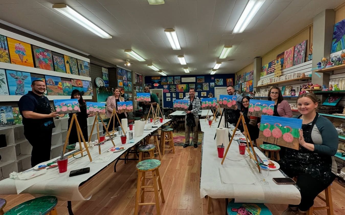 A group of people are sitting at long tables in a painting studio.