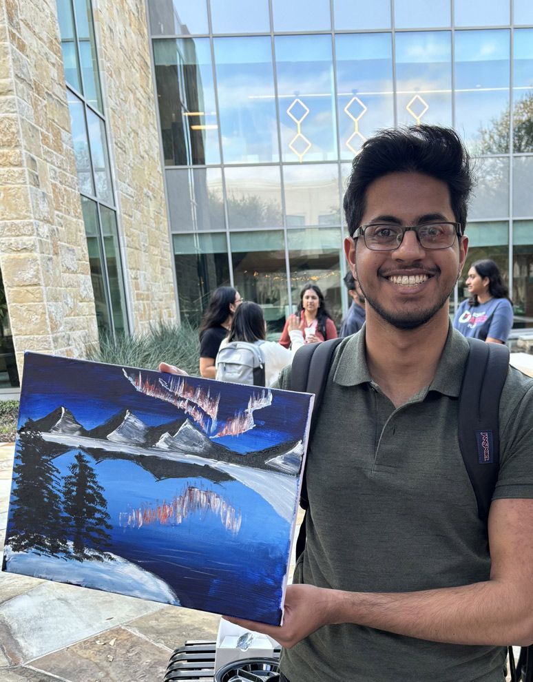 A man is holding a painting of a lake in front of a building.