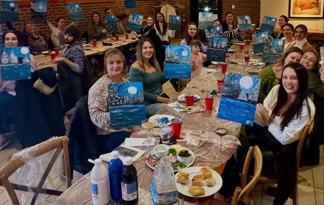Group of people at a painting party; holding paintings with a moonlit scene.