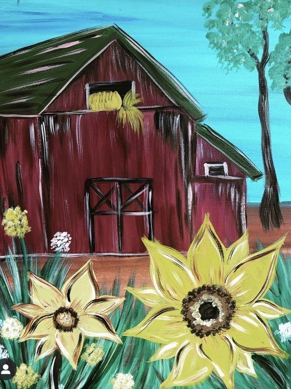 Red barn with flowers in front, against a bright blue sky and trees.