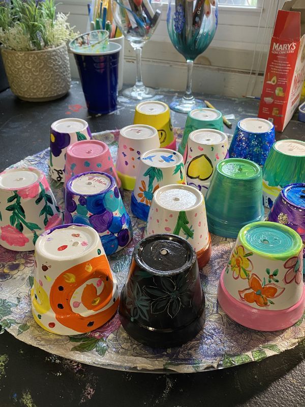 Colorful upside-down painted vases drying on a round table, with assorted craft supplies in the background
