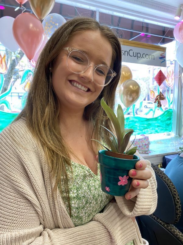 Smiling person holding a cup with a straw, standing indoors with balloons and colorful party decor.
