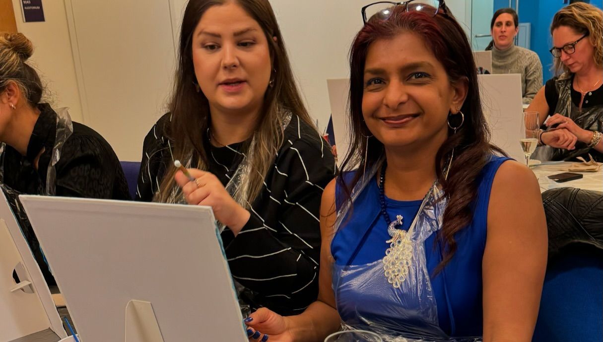Two women are sitting at a table looking at a laptop computer.