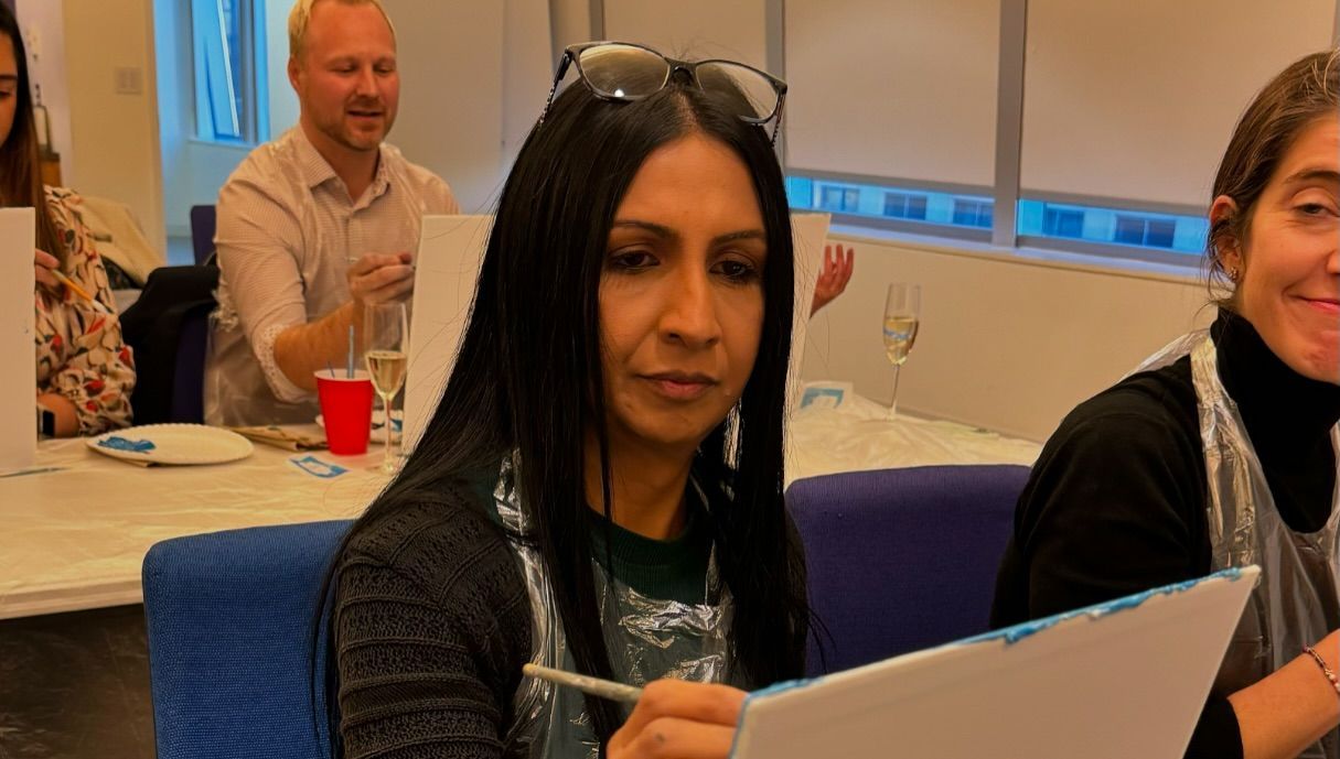 A woman is sitting at a table drawing on a piece of paper.