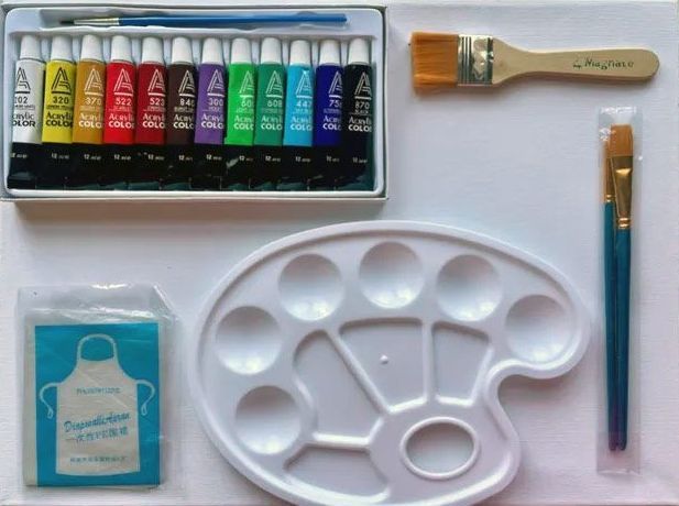 A box of acrylic paints a palette a brush and an apron