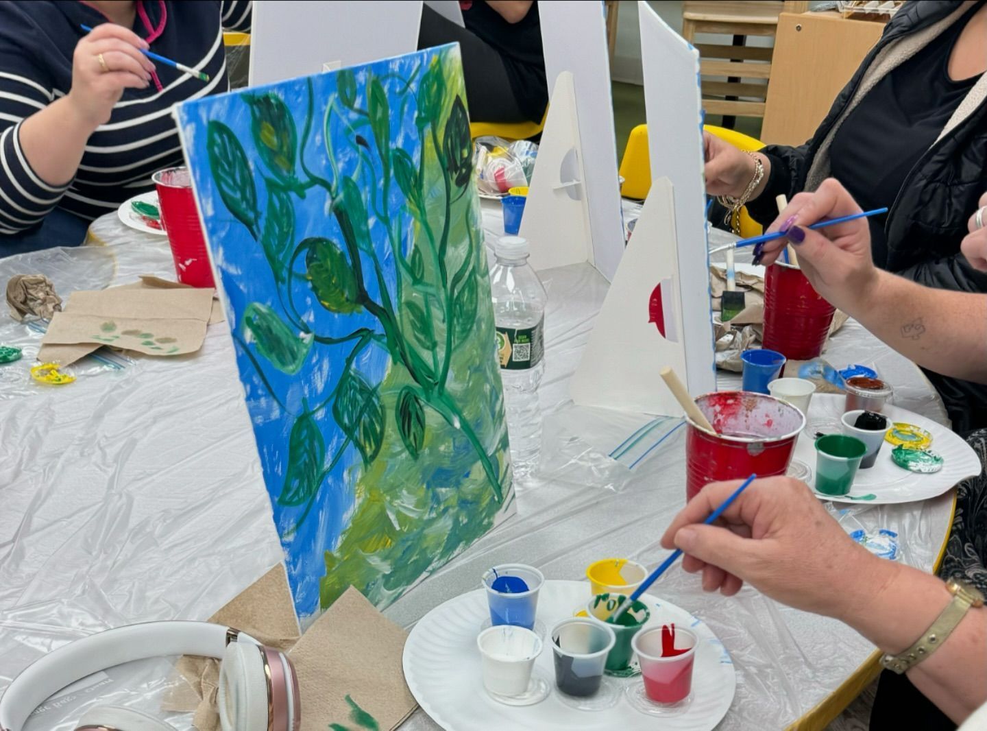 A group of people are sitting at a table painting on canvases.