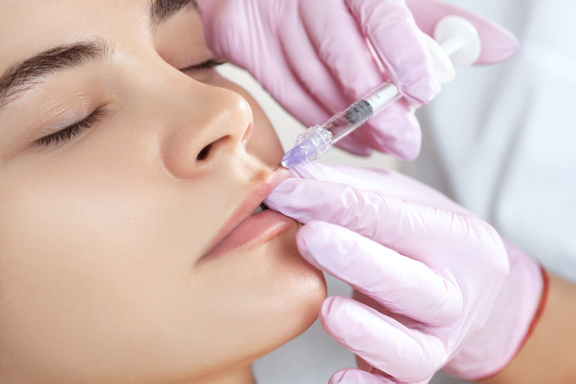 Gloved hands inject filler into a woman's lips during a cosmetic procedure