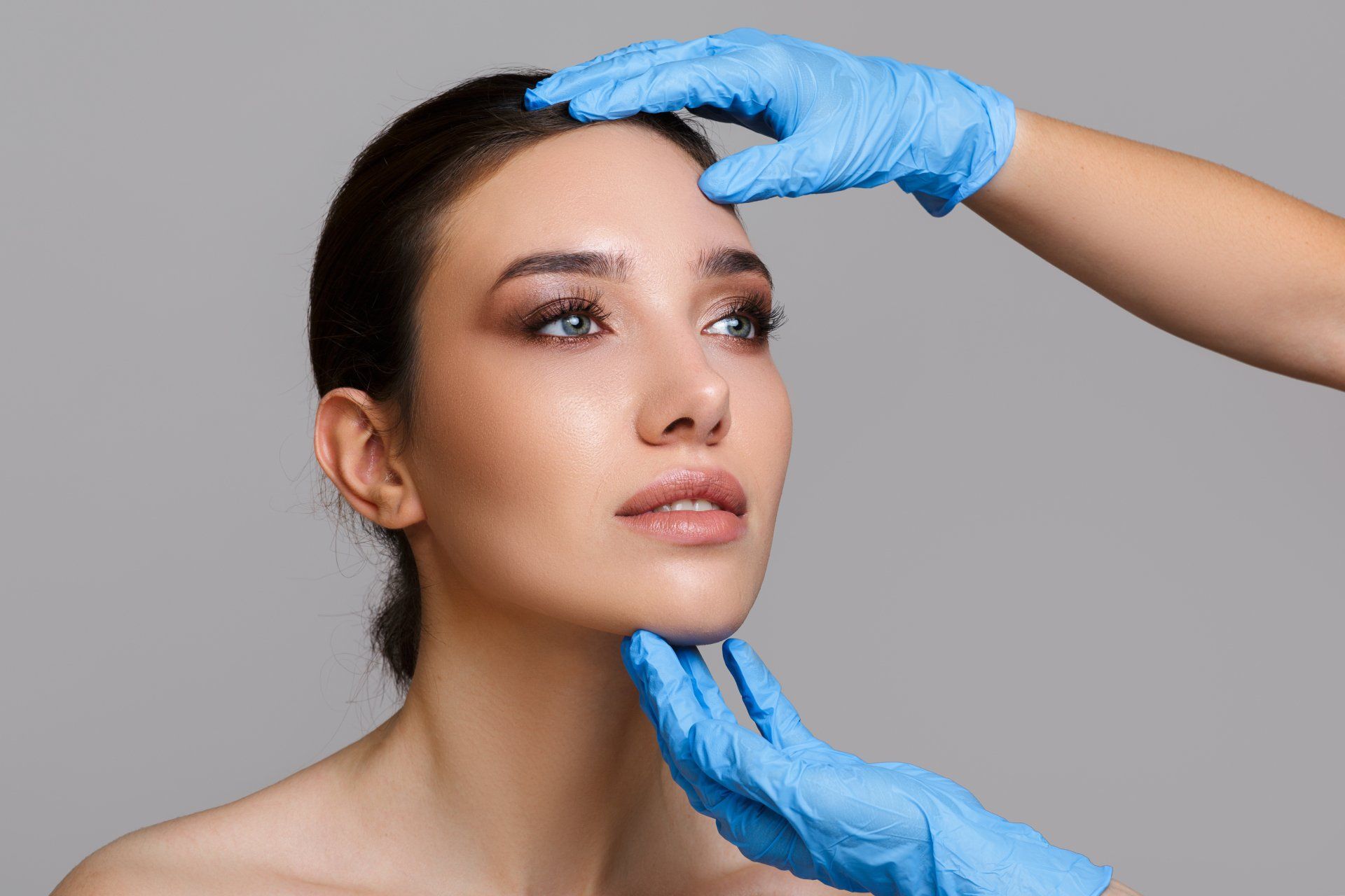Gloved hands shaping a woman’s face during a cosmetic treatment