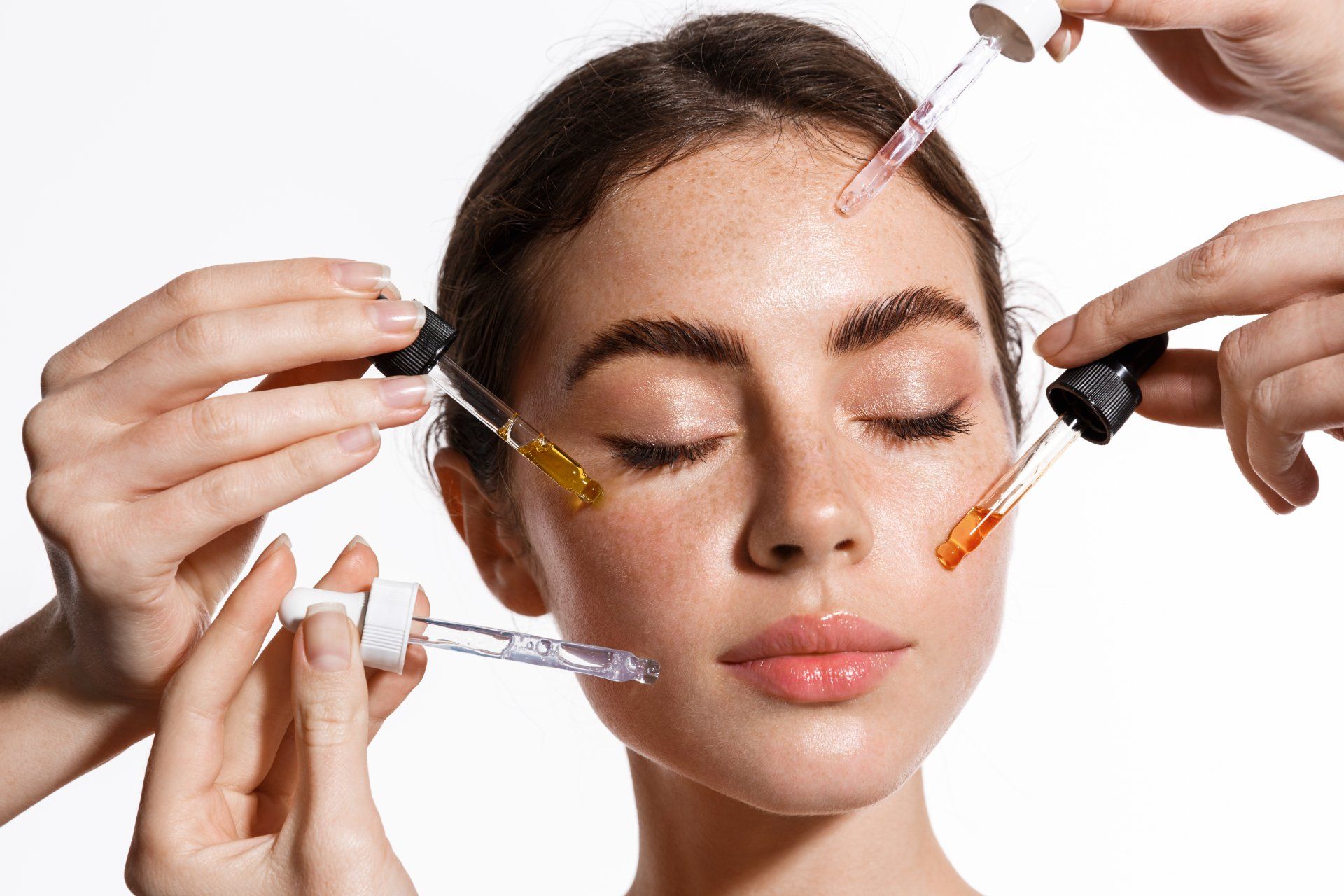 Hands applying facial serums with droppers to a woman’s face, spa treatment close-up