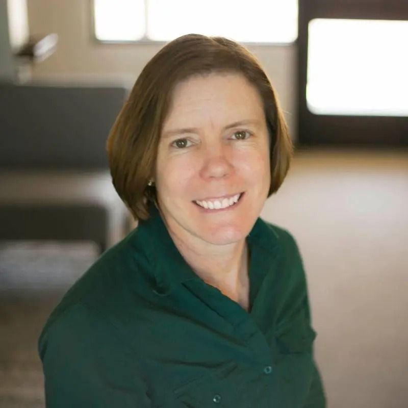 Woman with short brown hair smiles, wearing a green shirt.