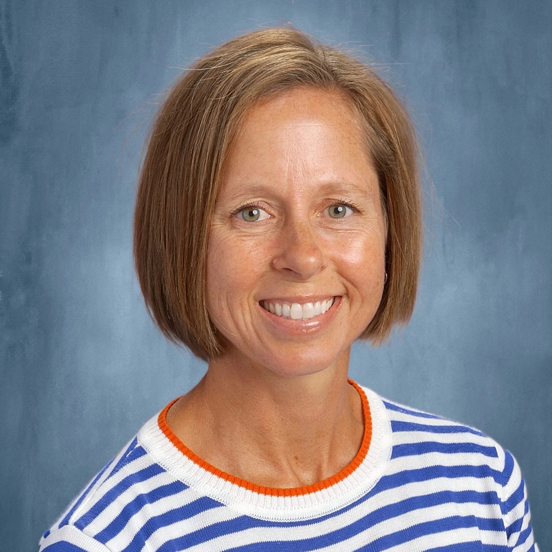 Woman with short brown hair, smiling, wearing a blue and white striped shirt.