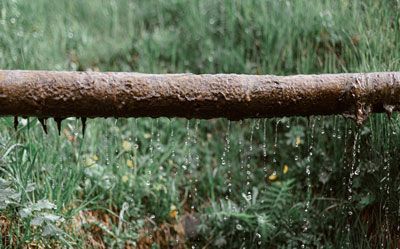 water is dripping from a rusty sewer pipe in the grass