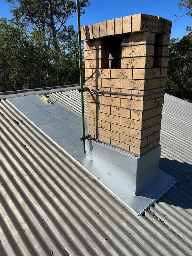 A Brick Chimney is Sitting on Top of a Corrugated Metal Roof — Peak Plumbing and Gas Fitting in Yamba, NSW