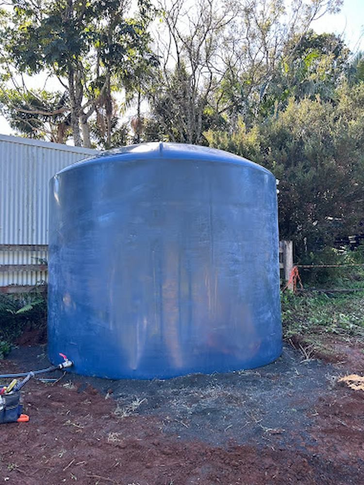 A Large Blue Water Tank is Sitting in the Dirt in Front of a Building — Peak Plumbing and Gas Fitting in Yamba, NSW