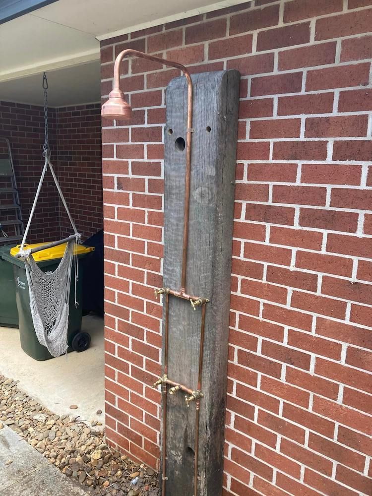 A Brick Wall With a Wooden Post With a Shower Head Attached to It — Peak Plumbing and Gas Fitting in Yamba, NSW