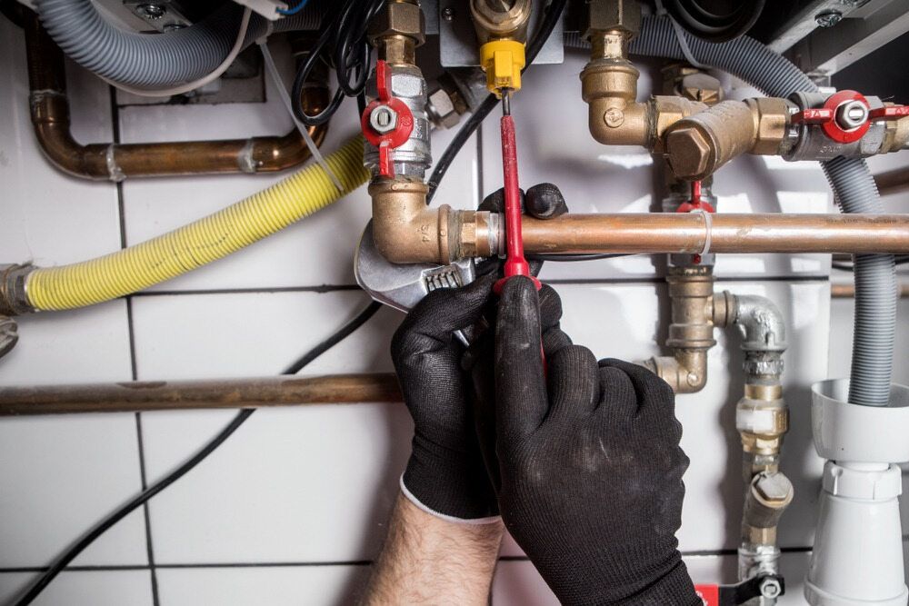 A Man is Fixing a Pipe With a Wrench in a Bathroom — Peak Plumbing and Gas Fitting in Yamba, NSW