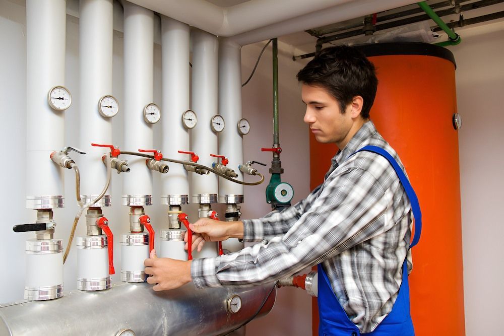 A Man is Working on a Boiler in a Boiler Room — Peak Plumbing and Gas Fitting in Yamba, NSW