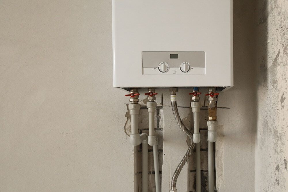 A White Boiler is Hanging on a Wall With Pipes Attached to It — Peak Plumbing and Gas Fitting in Iluka, NSW