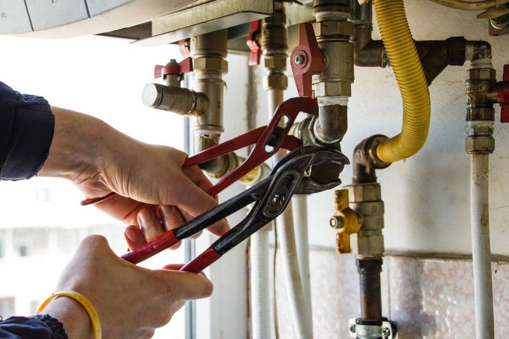 A Person is Fixing a Boiler With a Pair of Pliers — Peak Plumbing and Gas Fitting in Maclean, NSW