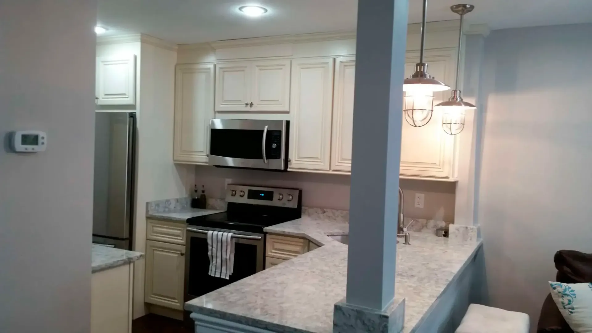 Open kitchen with white cabinets, granite countertops, stainless steel appliances, and pendant lights over a breakfast bar