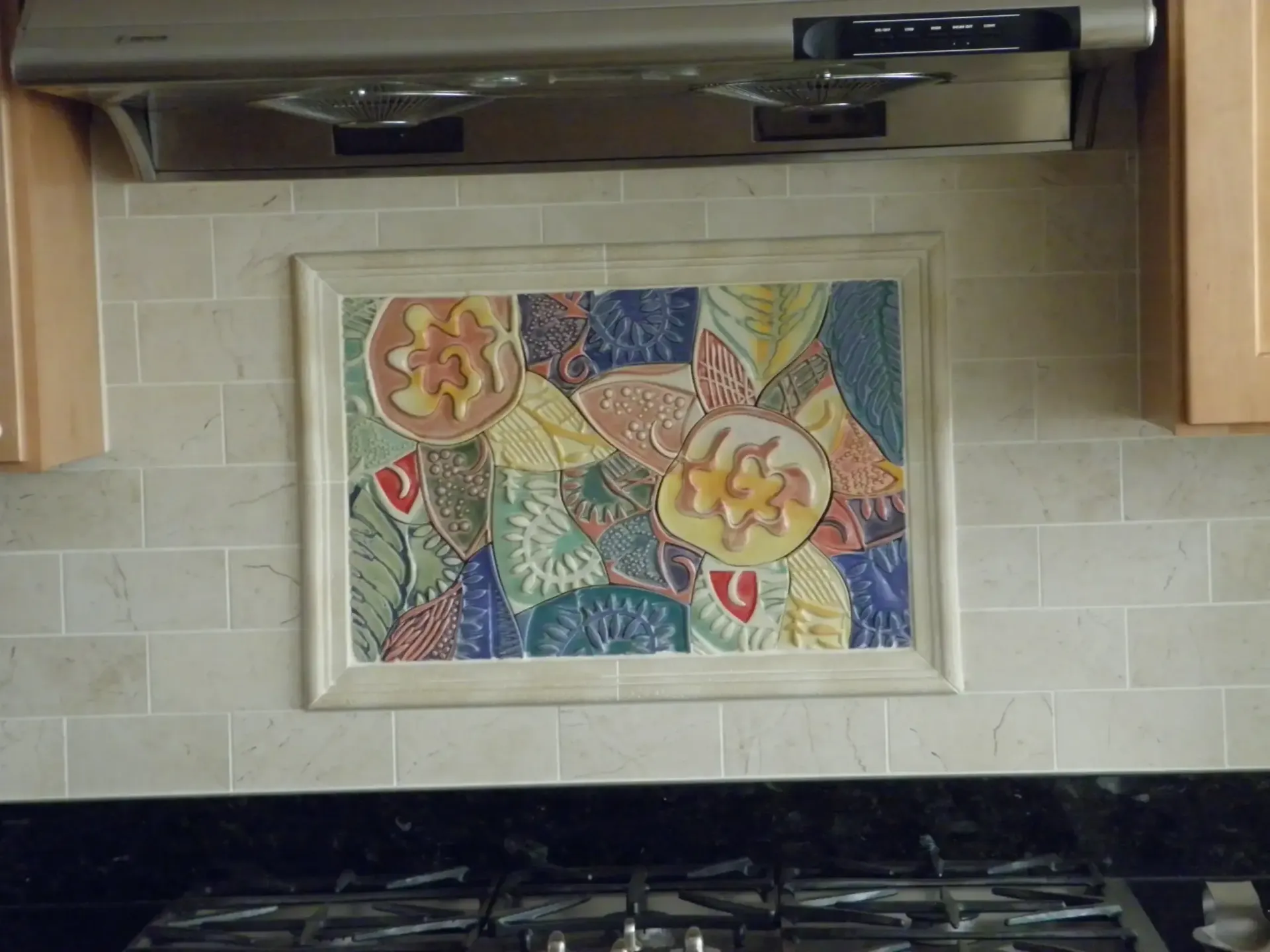Kitchen backsplash with colorful fruit tile mosaic beneath a stainless steel range hood
