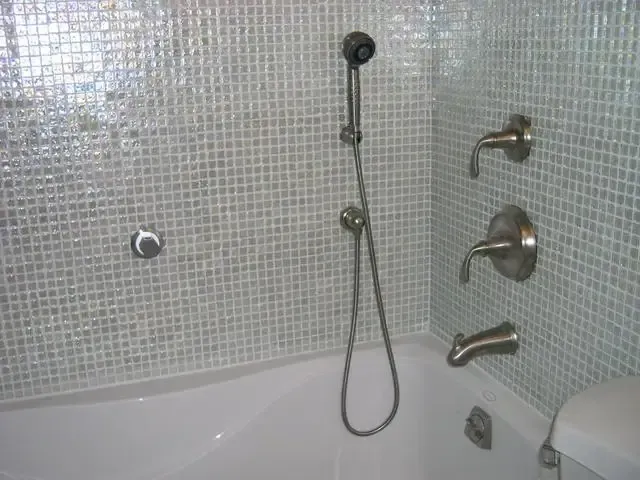 Modern bathroom with tiled walls, bathtub, handheld shower, wall faucet, and grab bars