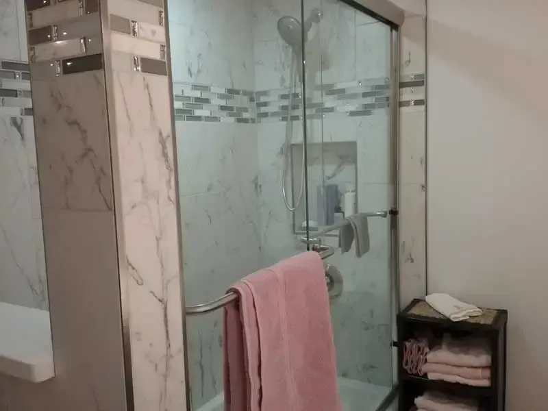 Modern bathroom with glass shower, marble tile, and a pink towel on the railing