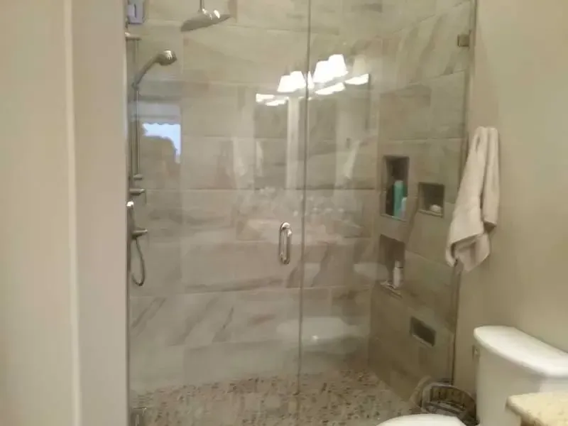 Modern walk-in shower with glass door, beige tile walls, pebble floor, and a white towel hanging nearby