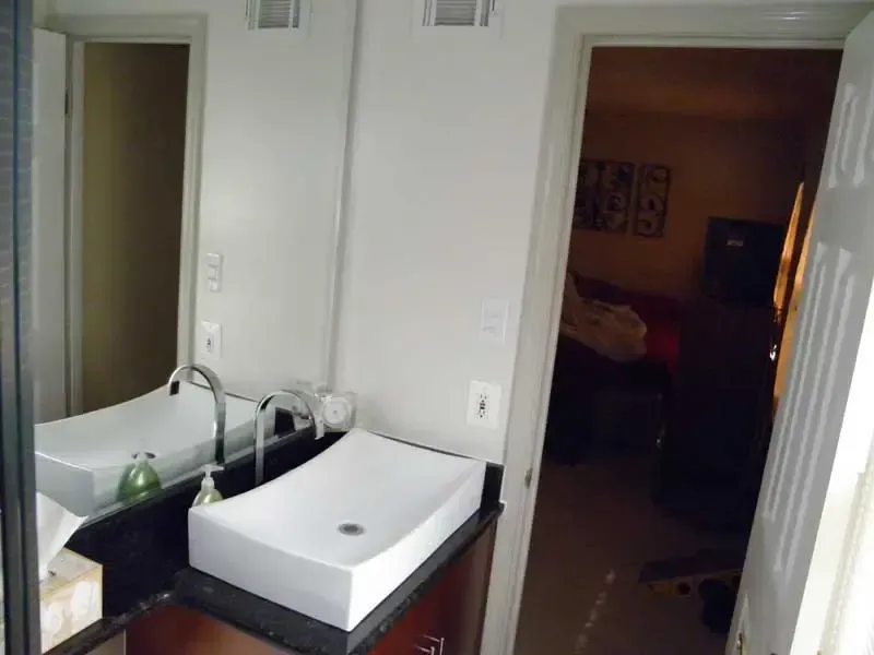 Bathroom with sink, mirror, and open doorway to a dimly lit room beyond.