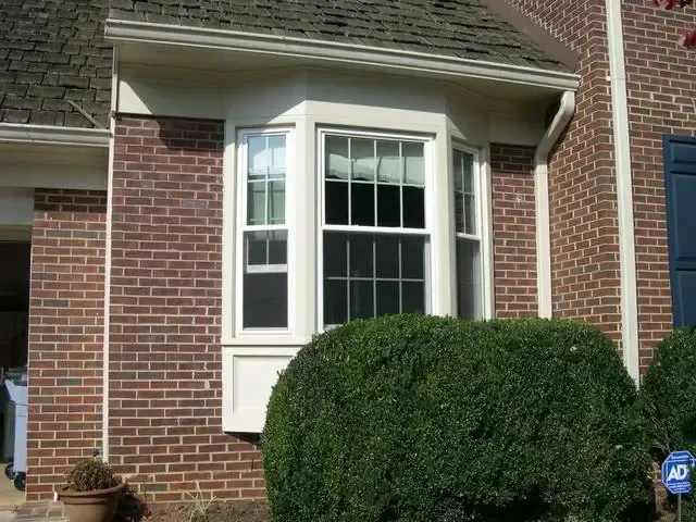 Brick house exterior with white bay window and trimmed bushes in front
