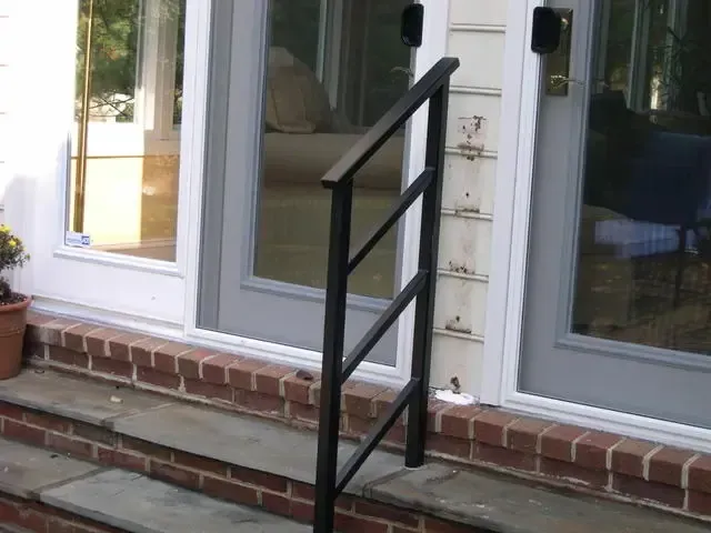 Black metal handrail on brick steps leading to a glass-front house entrance.