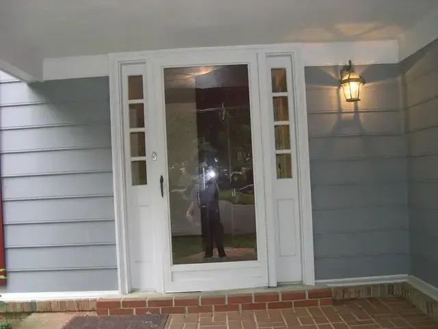 Front porch with white double doors, gray siding, and a lit wall lantern.