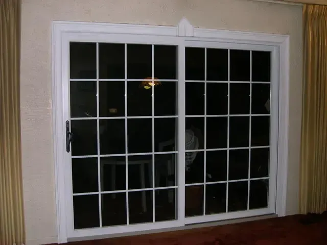 White sliding glass door with grid panes set in a beige wall at night