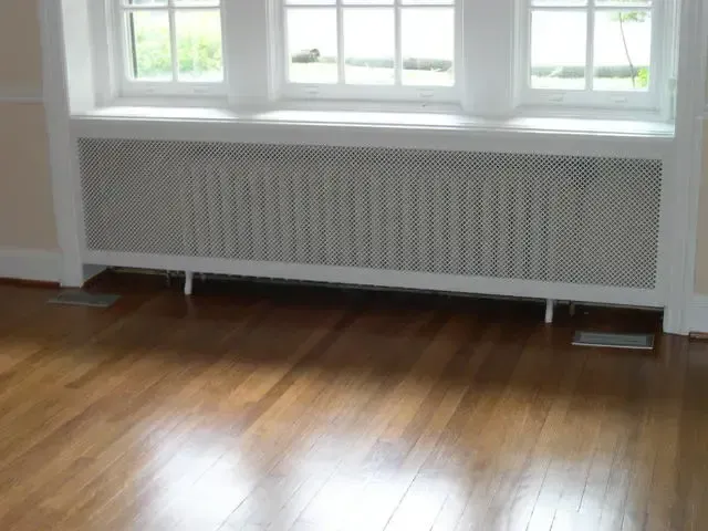 Empty room with hardwood floor, large windows, and a white radiator cover beneath the windows.