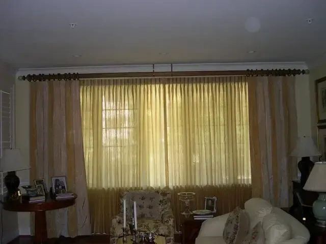 Living room with large curtained window, sofa, side tables, and lamps in soft daylight