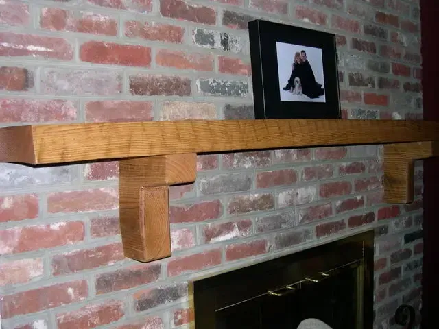 Wooden fireplace mantel on a brick wall with a framed photo above the hearth.
