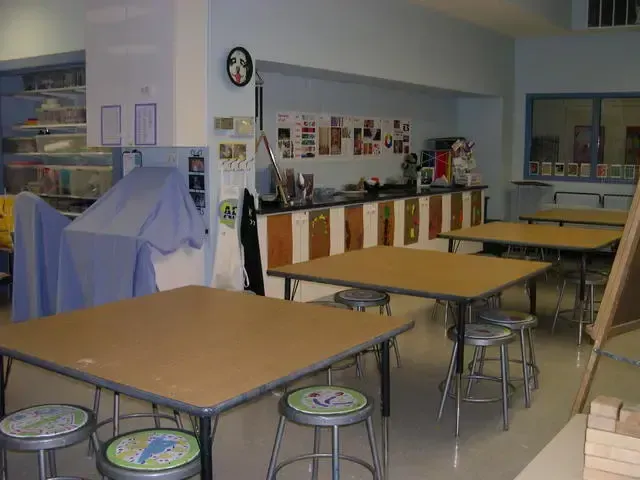 Empty classroom with tables, stools, and a covered object near the wall