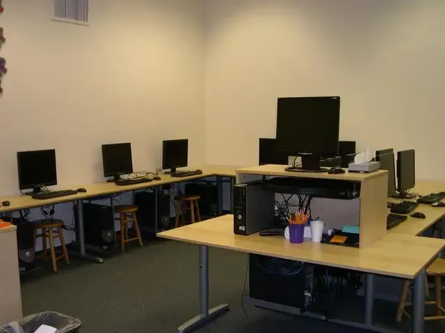 Computer lab with several desktop monitors on wooden desks and a large monitor in the foreground.