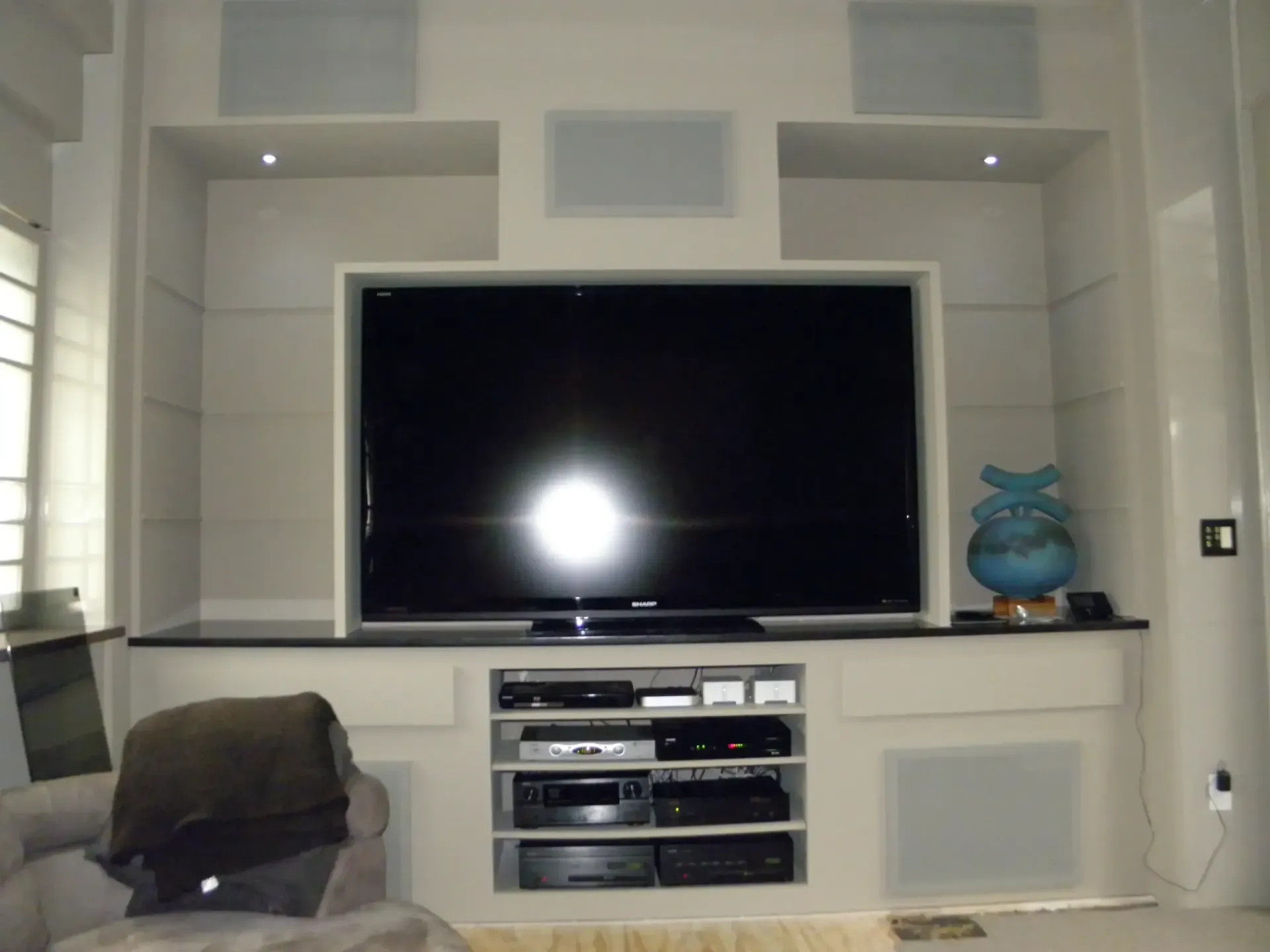 Living room wall with large flat-screen TV, built-in shelves, and a blue vase on the right side.