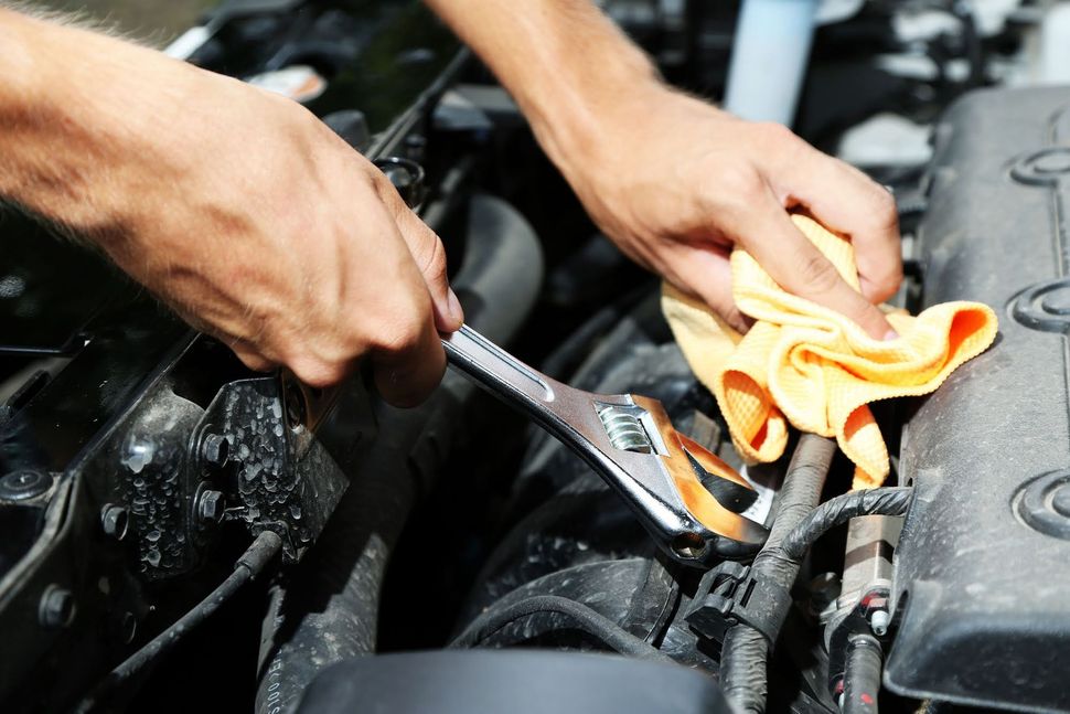Mani che puliscono e riparano un motore d'auto con un panno e una chiave a cricchetto.