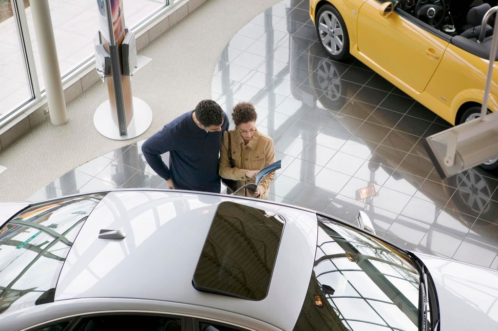 Due persone che sfogliano una brochure di un'auto accanto a una vettura bianca in uno showroom luminoso.