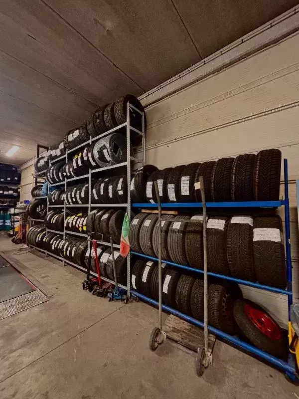 Scaffalatura per pneumatici in un garage, con file di pneumatici neri su ripiani blu e pavimento in cemento.