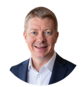 Studio headshot of a smiling man in a navy blazer and white shirt on a white background