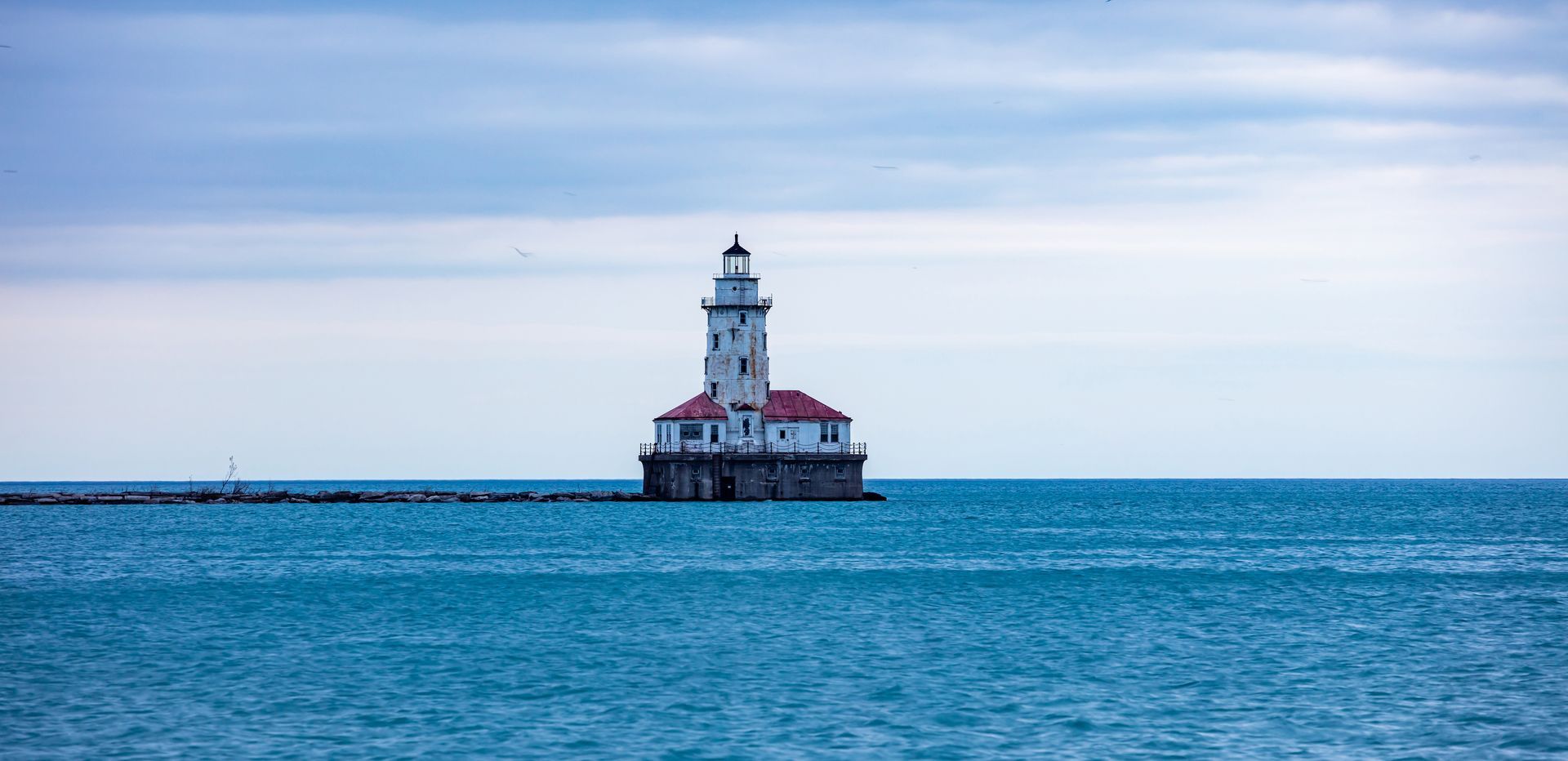 Lighthouse on a small island in calm blue water under a pale cloudy sky