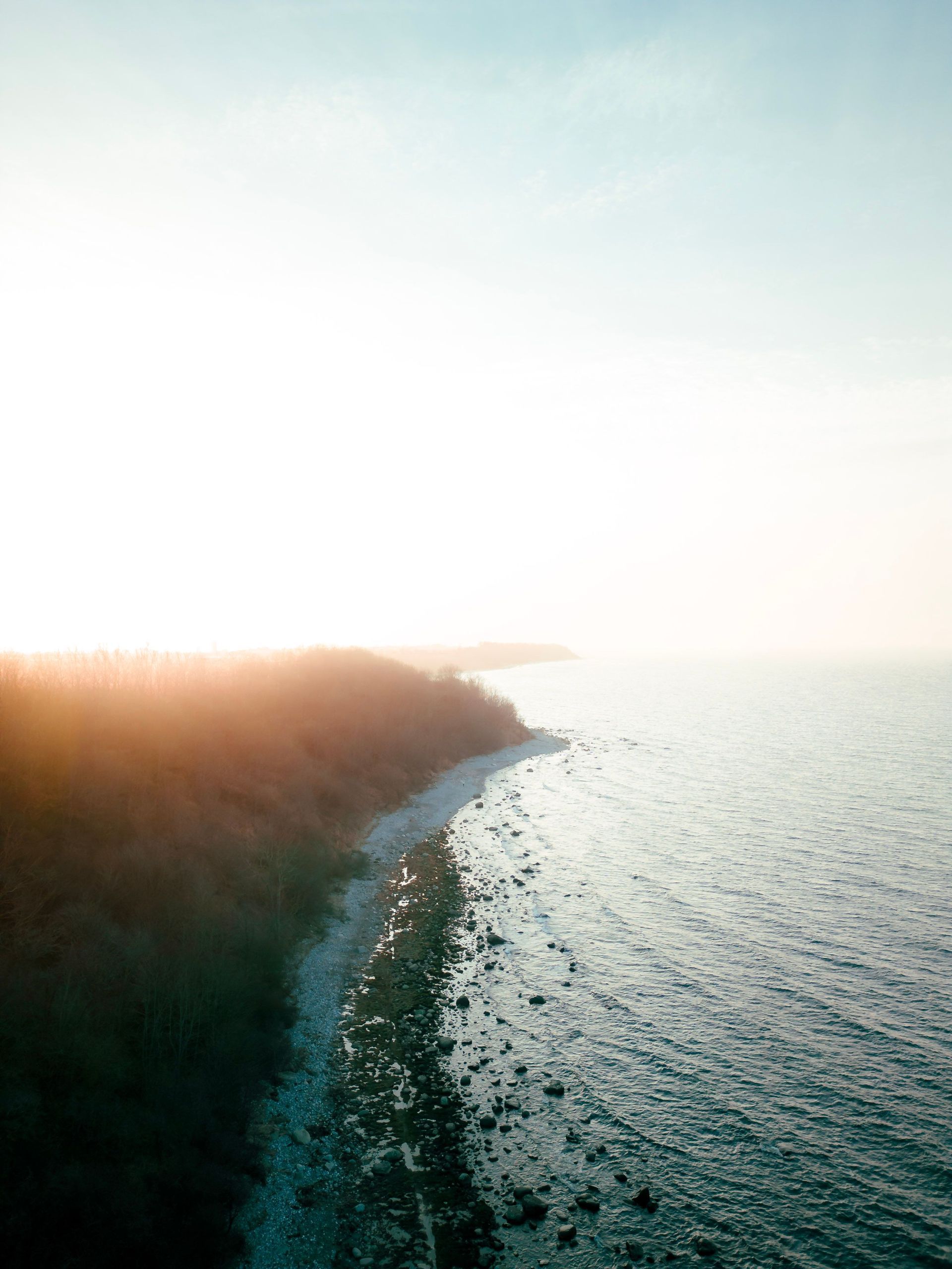 Sunlit coastline with waves beside a rocky shore at sunrise