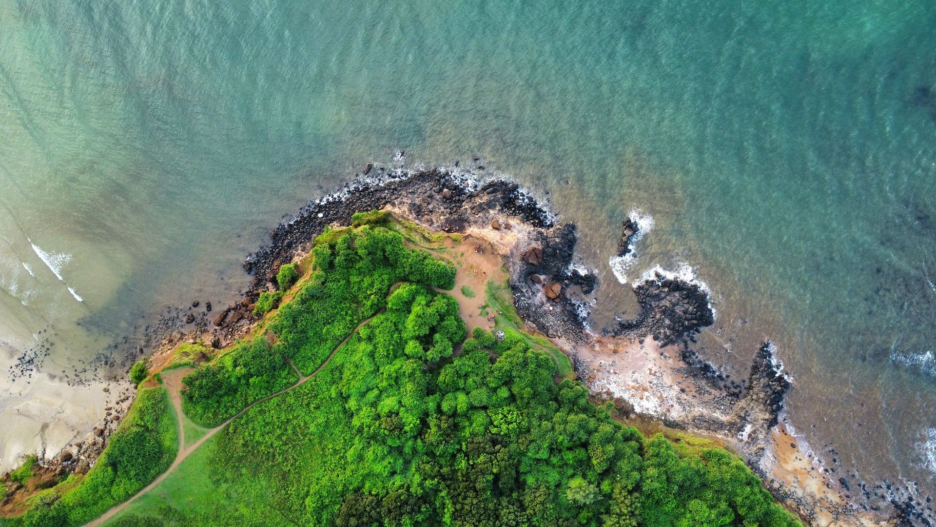 Aerial view of a green rocky shoreline meeting turquoise water and white waves