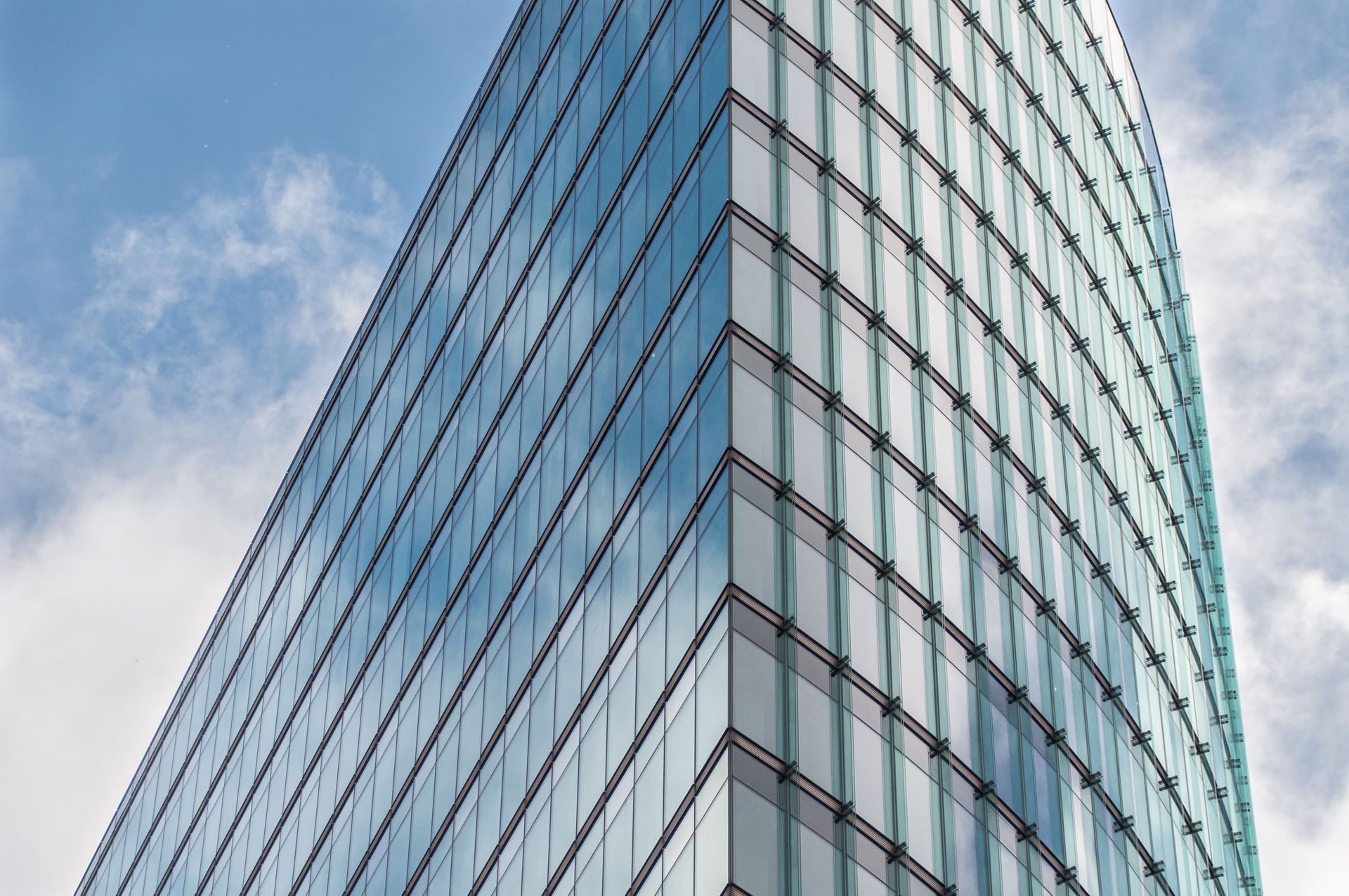 Curved glass office building corner against a blue sky with clouds