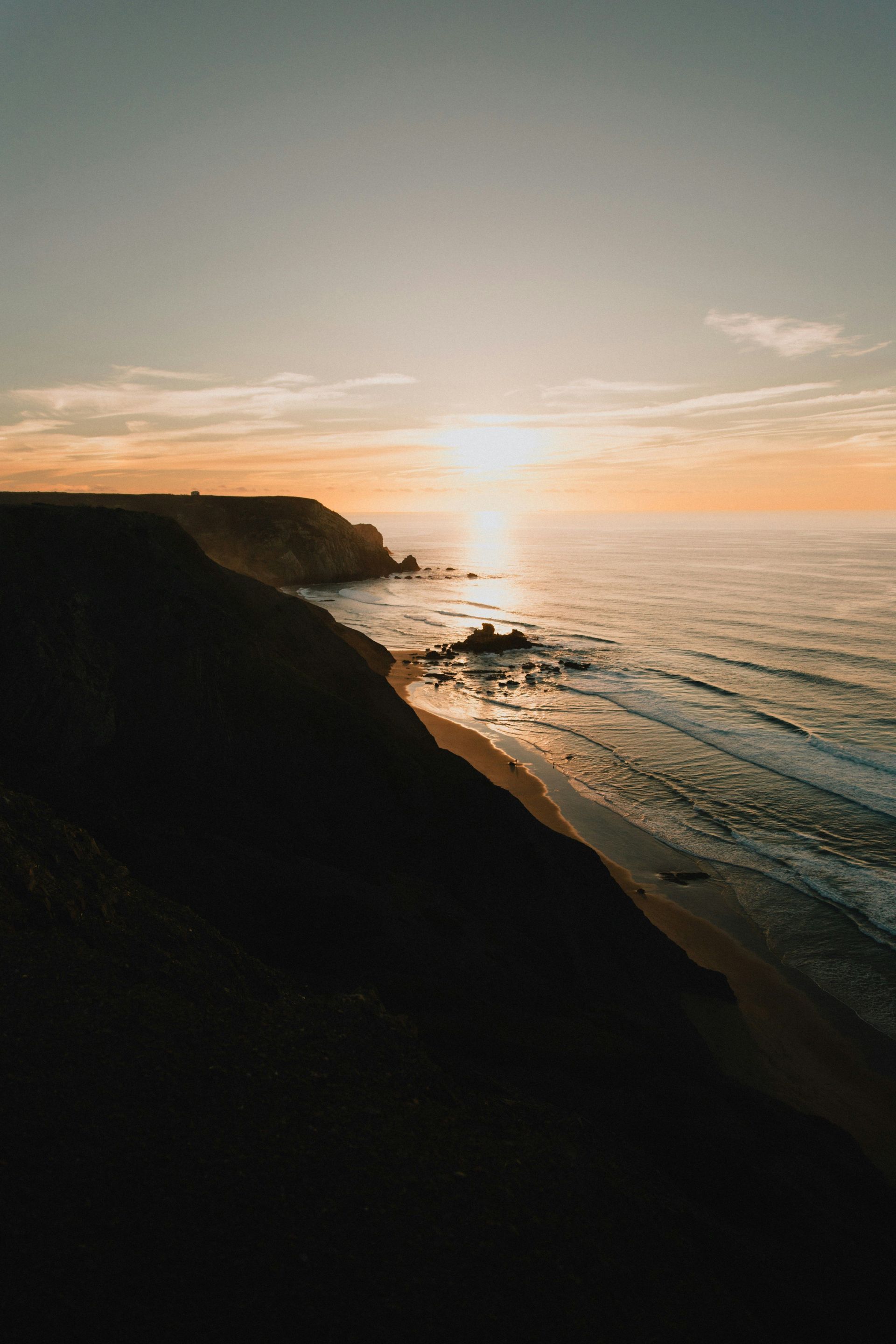 Sunset over a calm ocean with cliffs silhouetted in the foreground