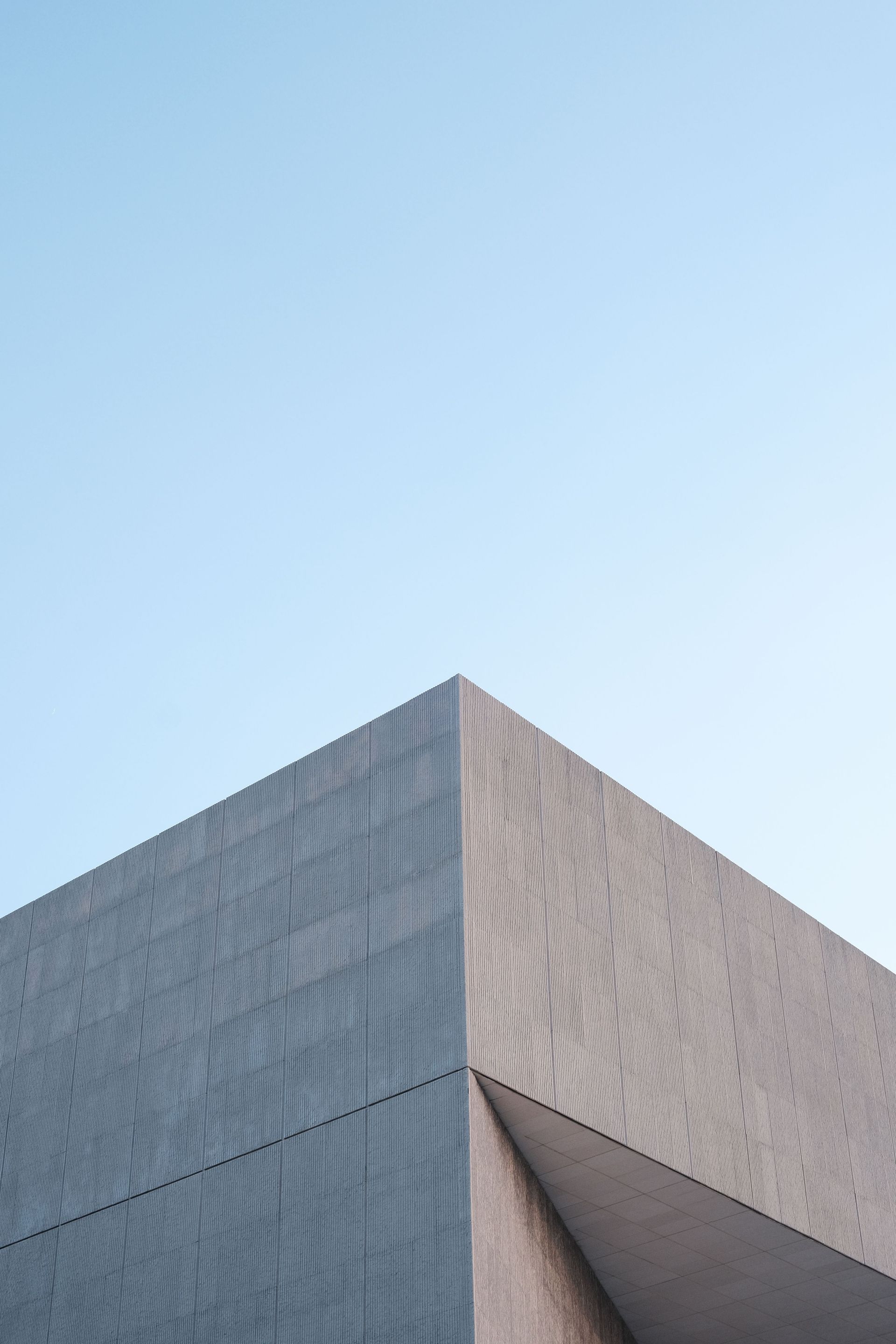 Close-up of a modern building corner with gray textured walls against a clear blue sky