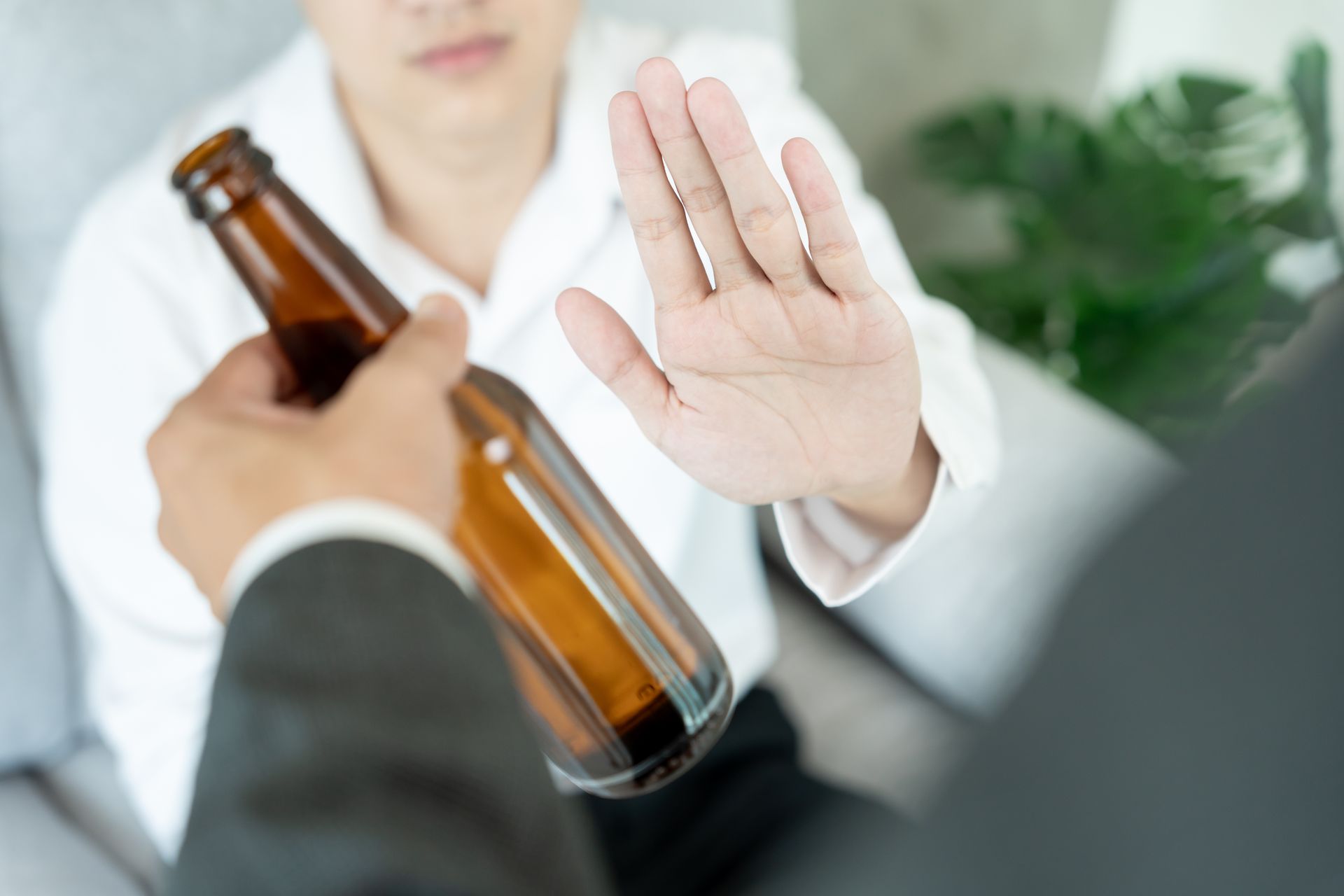 Person raising a hand to refuse an offered bottle while another hand holds a brown glass bottle. Person raising a hand to refuse an offered bottle while another hand holds a brown glass bottle.